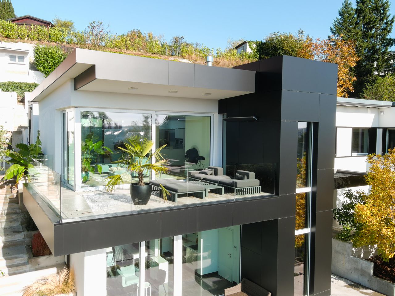 about-us-01 Contemporary house featuring glass balcony, lush plants, and stylish design.